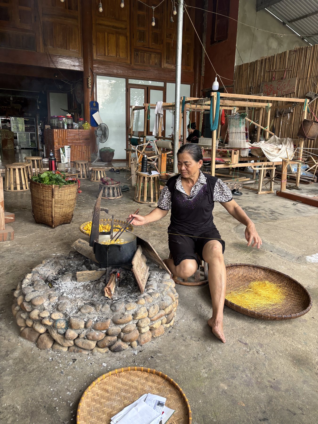 Cô Hoa dyeing silk over a wood fire in the courtyard of the weaving house
